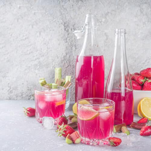 Erdbeer-Rhabarber-Limonade aus dem Thermomix® in zwei Gläsern und Flaschen, mit Erdbeeren