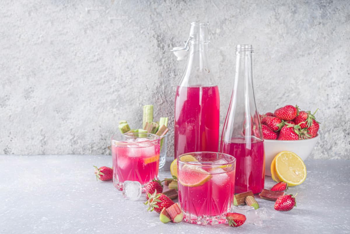 Erdbeer-Rhabarber-Limonade aus dem Thermomix® in zwei Gläsern und Flaschen, mit Erdbeeren
